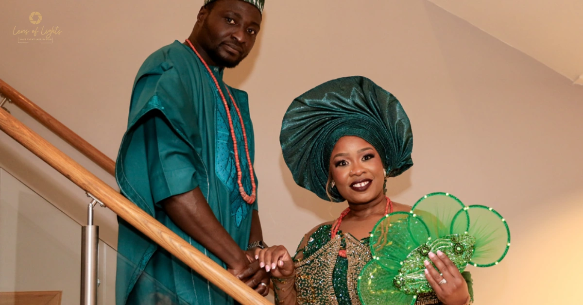 Nigerian couple in traditional Yoruba wedding attire standing on staircase, wearing green aso ebi with gele and agbada